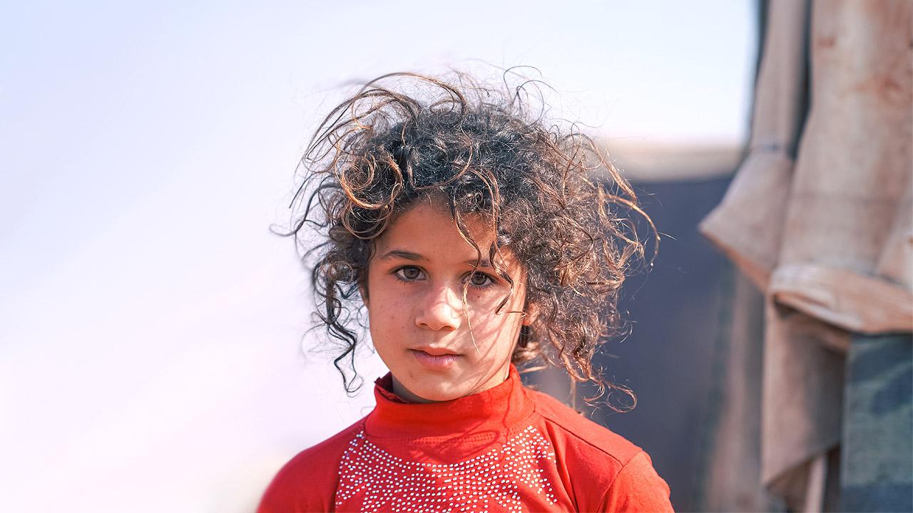 Ein Kind mit etwas zerzausten Haaren, im Hintergrund eine Art Zelt