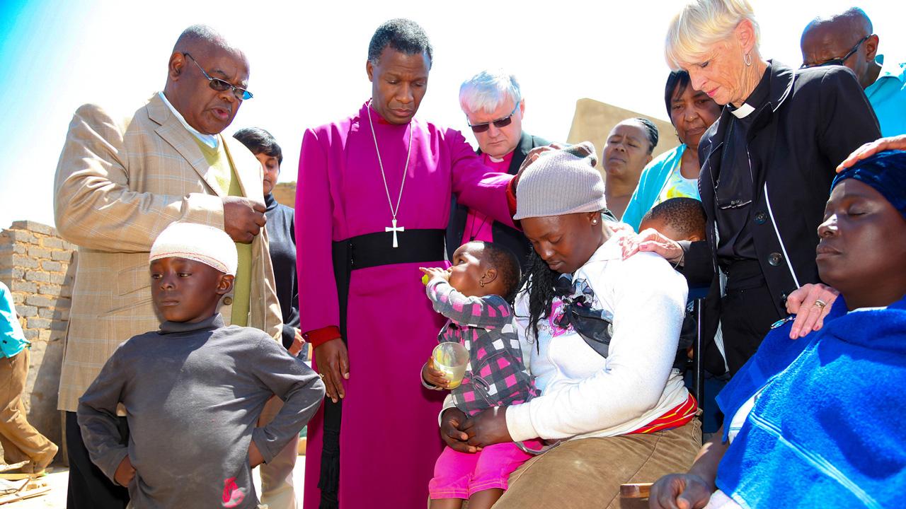 Ein Preises, ein Erzbischof, stehen zwischen ein paar Menschen, sie beten miteinander