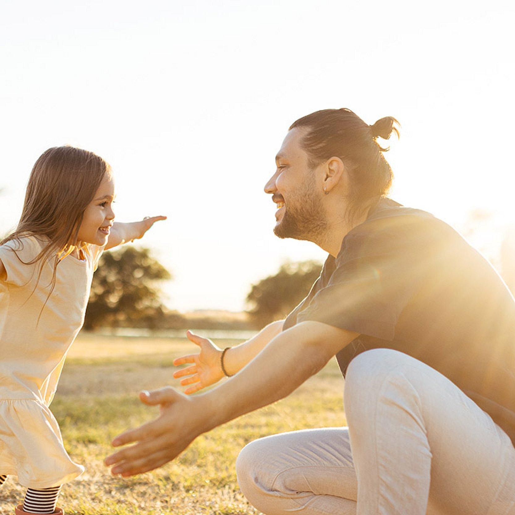 Ein Mädchen läuft auf ihren Vater zu, der die Arme ausbreitet