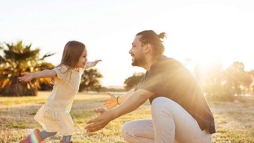 Ein Mädchen läuft auf ihren Vater zu, der die Arme ausbreitet