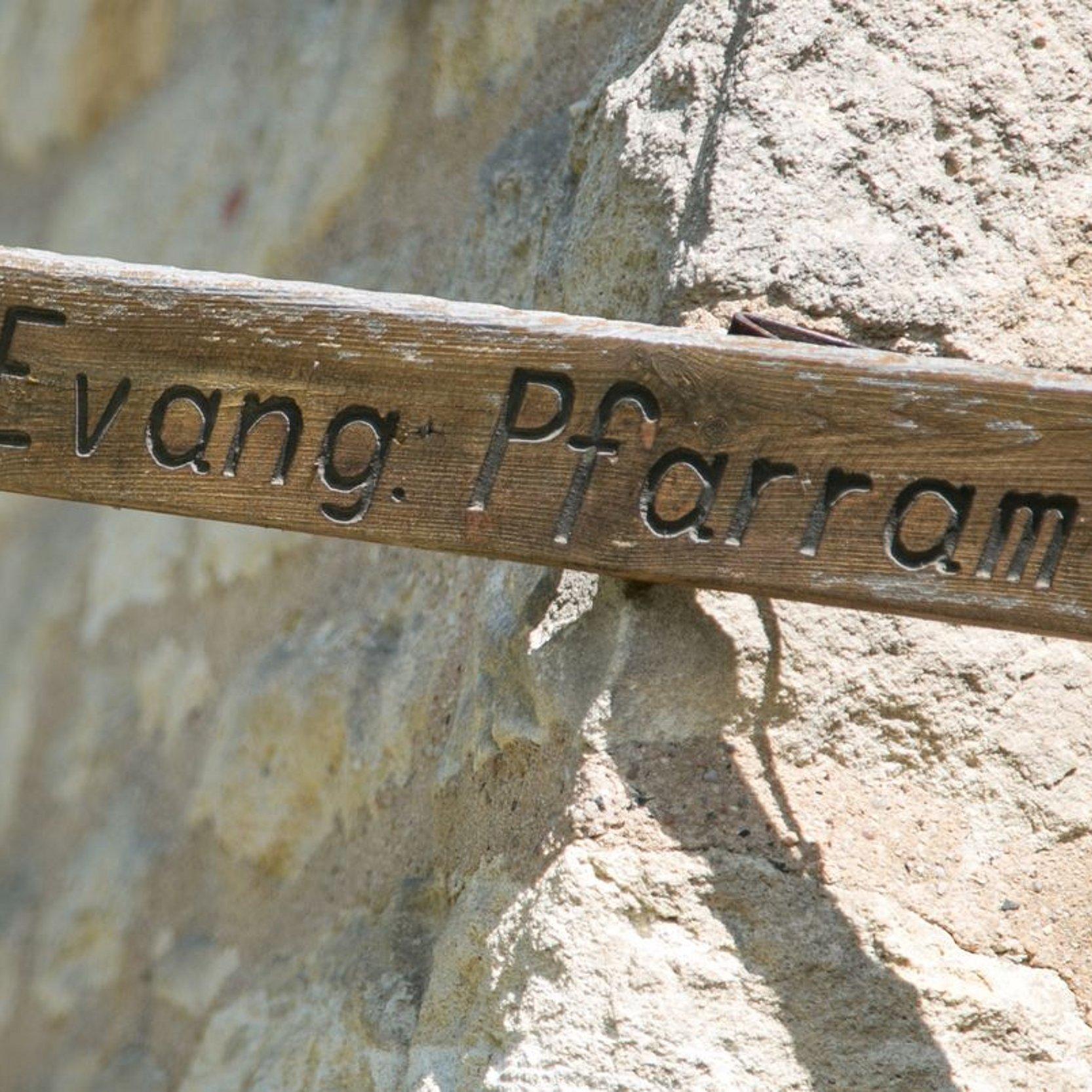 Holzpfeil mit Aufschrift "Evang. Pfarramt" an einer Natursteinwand