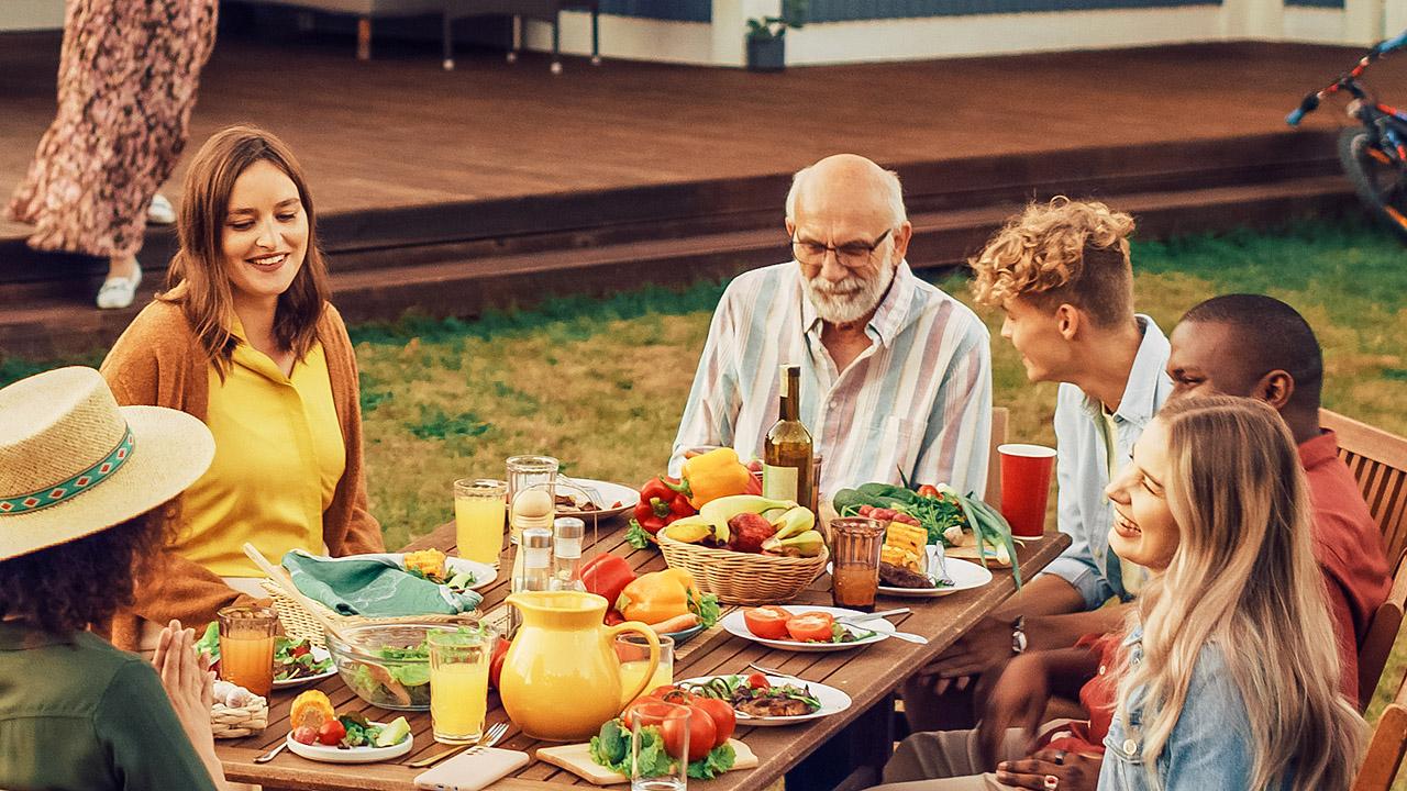 Eine Familie isst an einem Tisch im Garten, dabei auch ein schwerhöriger Großvater