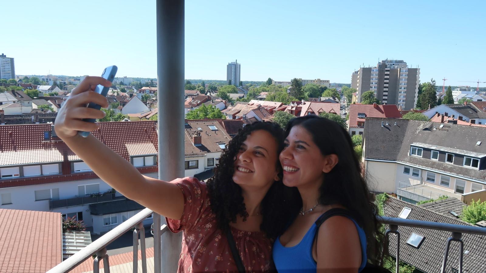 Zwei junge Frauen fotografieren sich selbst, im Hintergrund ist der Ort Neu-Isenburg zu sehen.