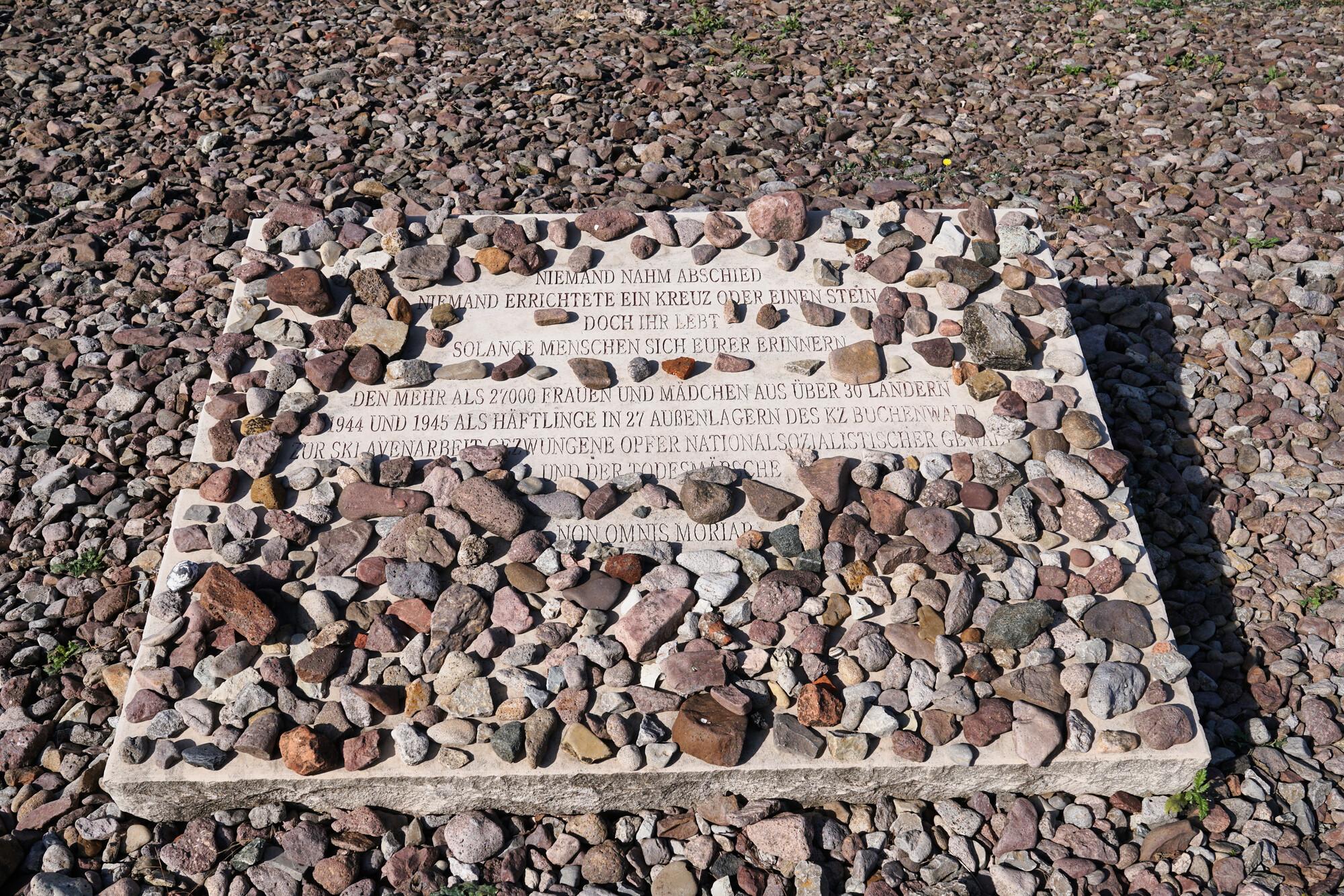 KZ Gedenkstätte Buchenwald. Eine Gedenkplatte mit Text liegt auf Kieselsteinen. 