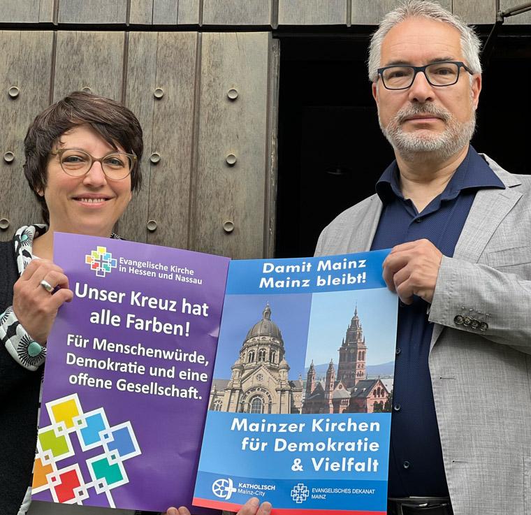 Pfarrerin Eva Lemaire und Dekan Andreas Klodt vor der Christuskirche Mainz halten Plakate in der Hand