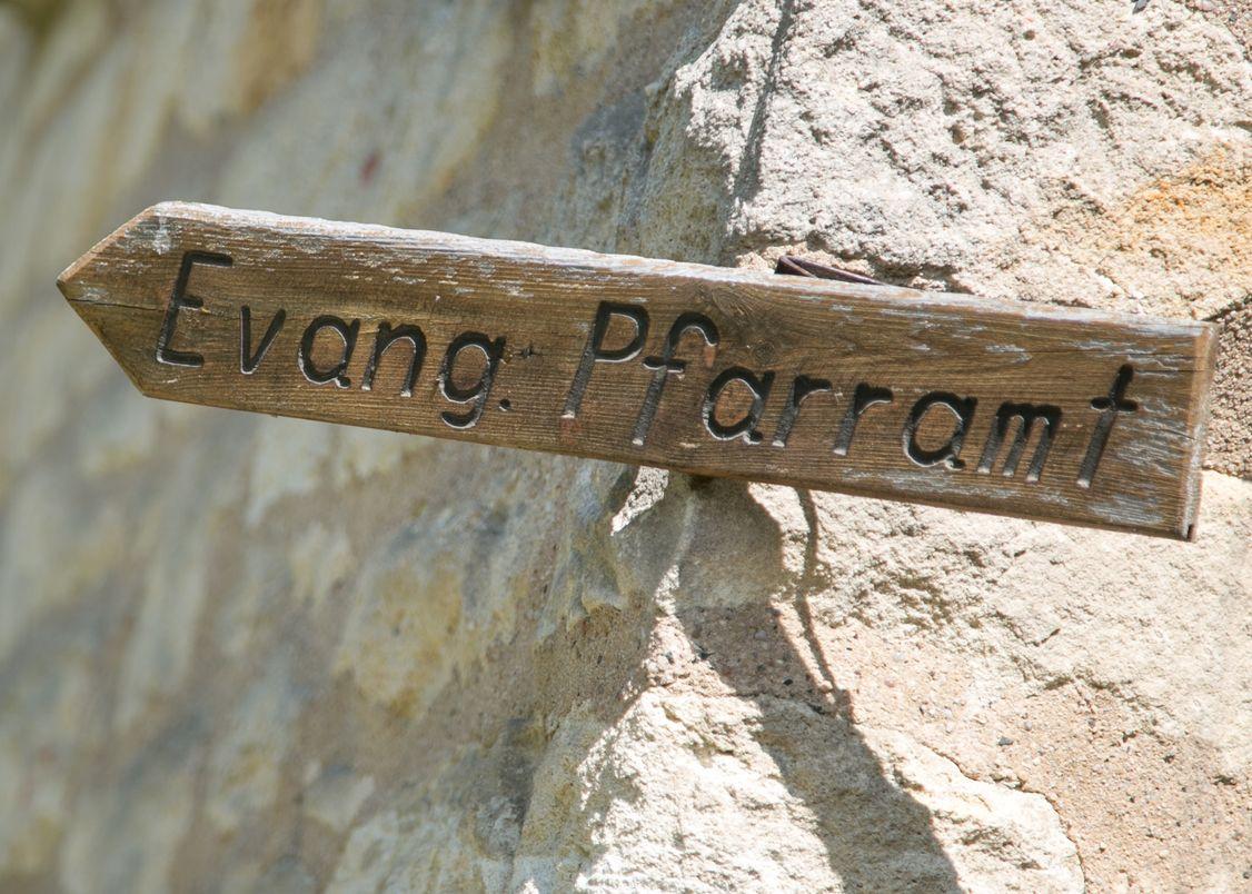 Holzpfeil mit Aufschrift "Evang. Pfarramt" an einer Natursteinwand