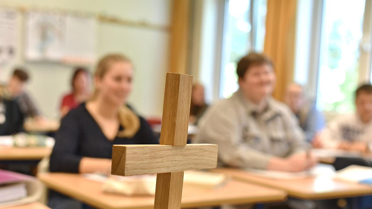 Holzkreuz vor Schülerinnen und Schülern im Unterricht