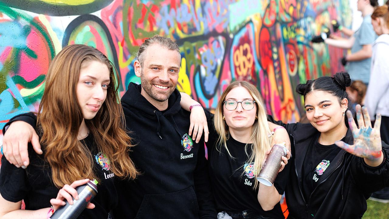 Eine Gruppe junger Erwachsener vor einer mit Graffiti gestaltenten Wand
