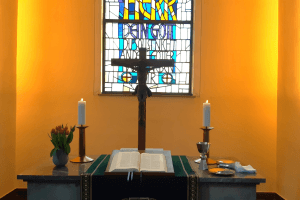 Altar der Stadtkirche, in der Mitte das Kreuz, davor die aufgeschlagene Bibel, rechts und links je eine brennende Kerze, ganz links ein Strauß roter Tulpen