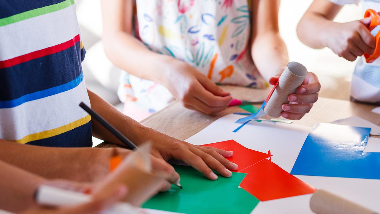 Basteln Kinderhände, die mit farbigen Papieren basteln