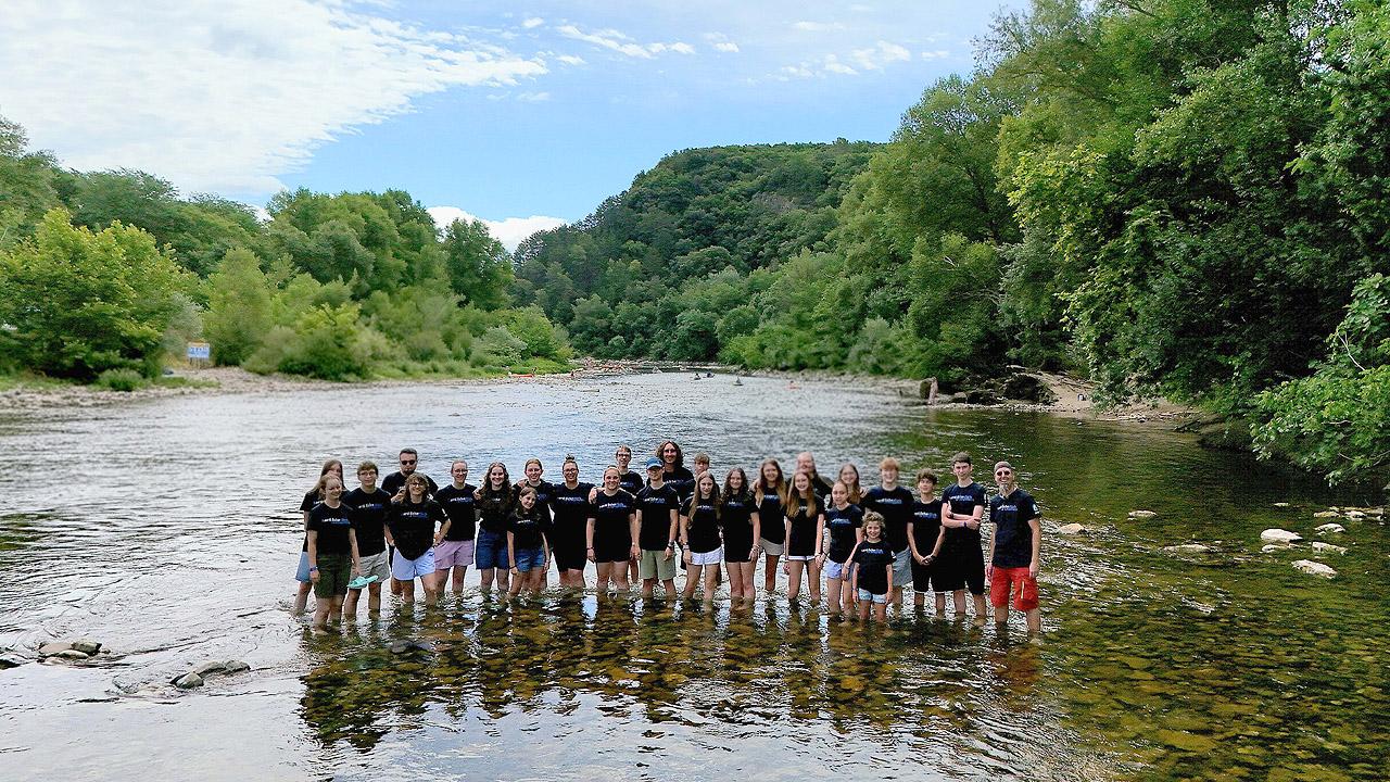 Jugendgruppe, die im flachen Wasser eines Flusses steht, dahinter Berge