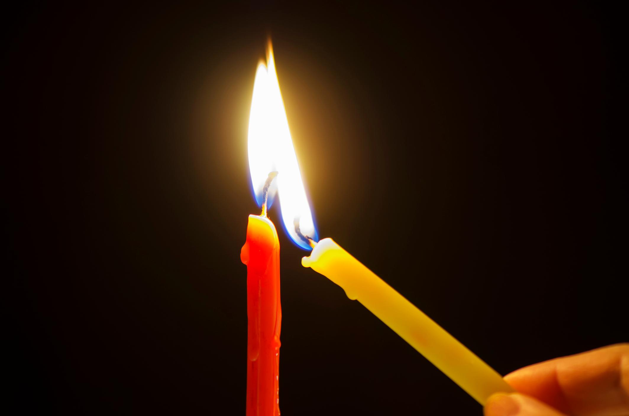 Segen geben und ein Licht empfangen Eine gelbe schmale Kerze wird an einer roten schmalen Kerze angezündet.