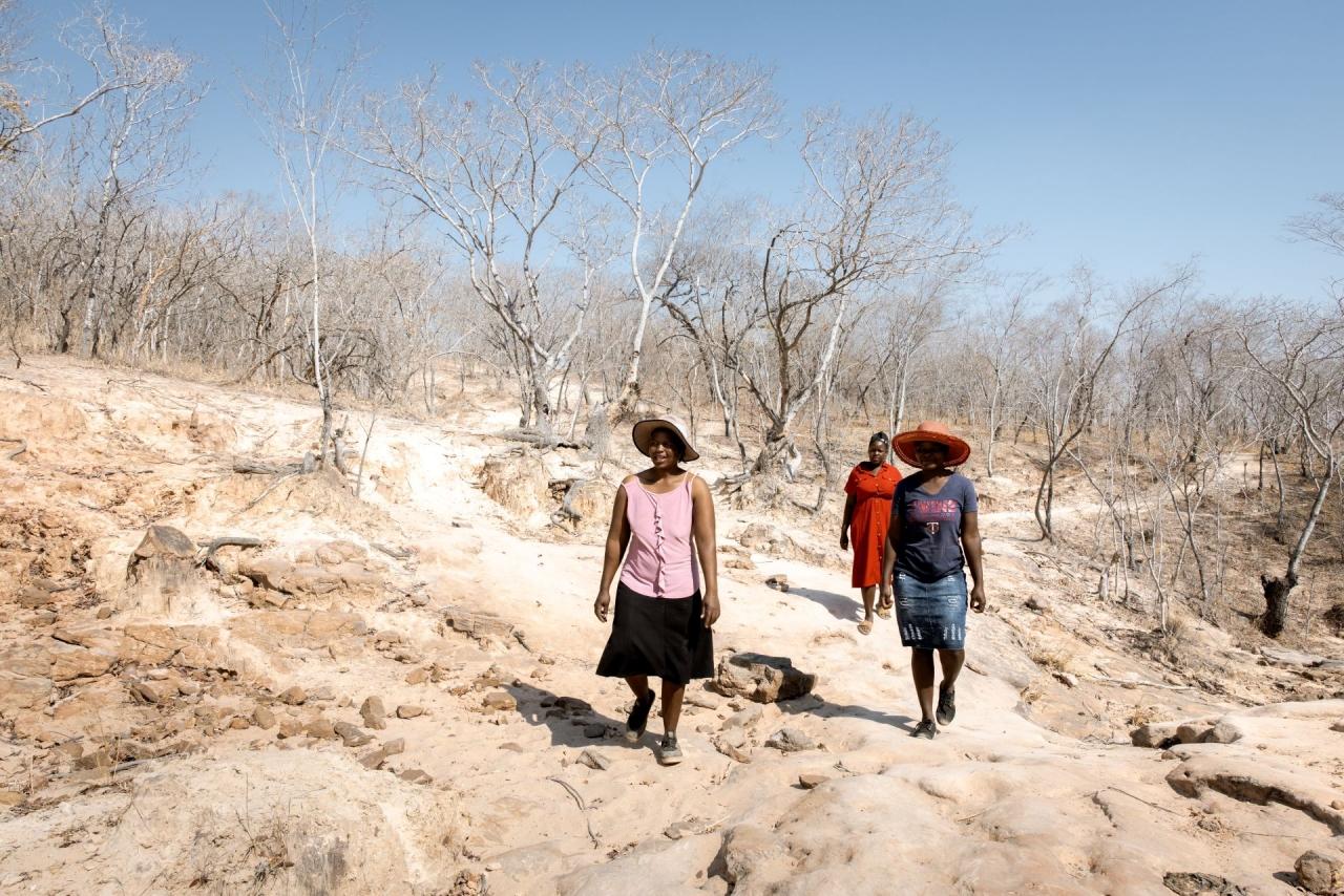 Drei Frauen gehen in karger Landschaft.
