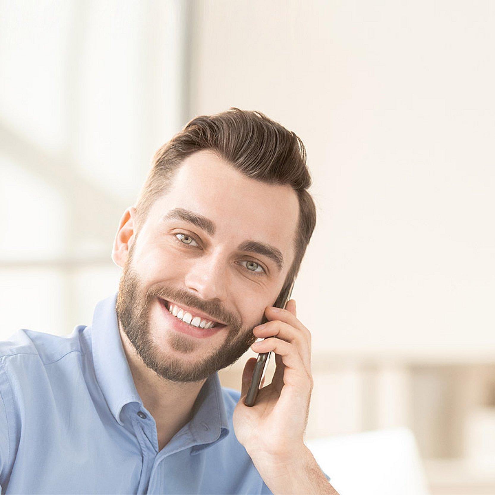 Verwaltungsmitarbeitende Ein Mann in hellblauem Hemd telefoniert