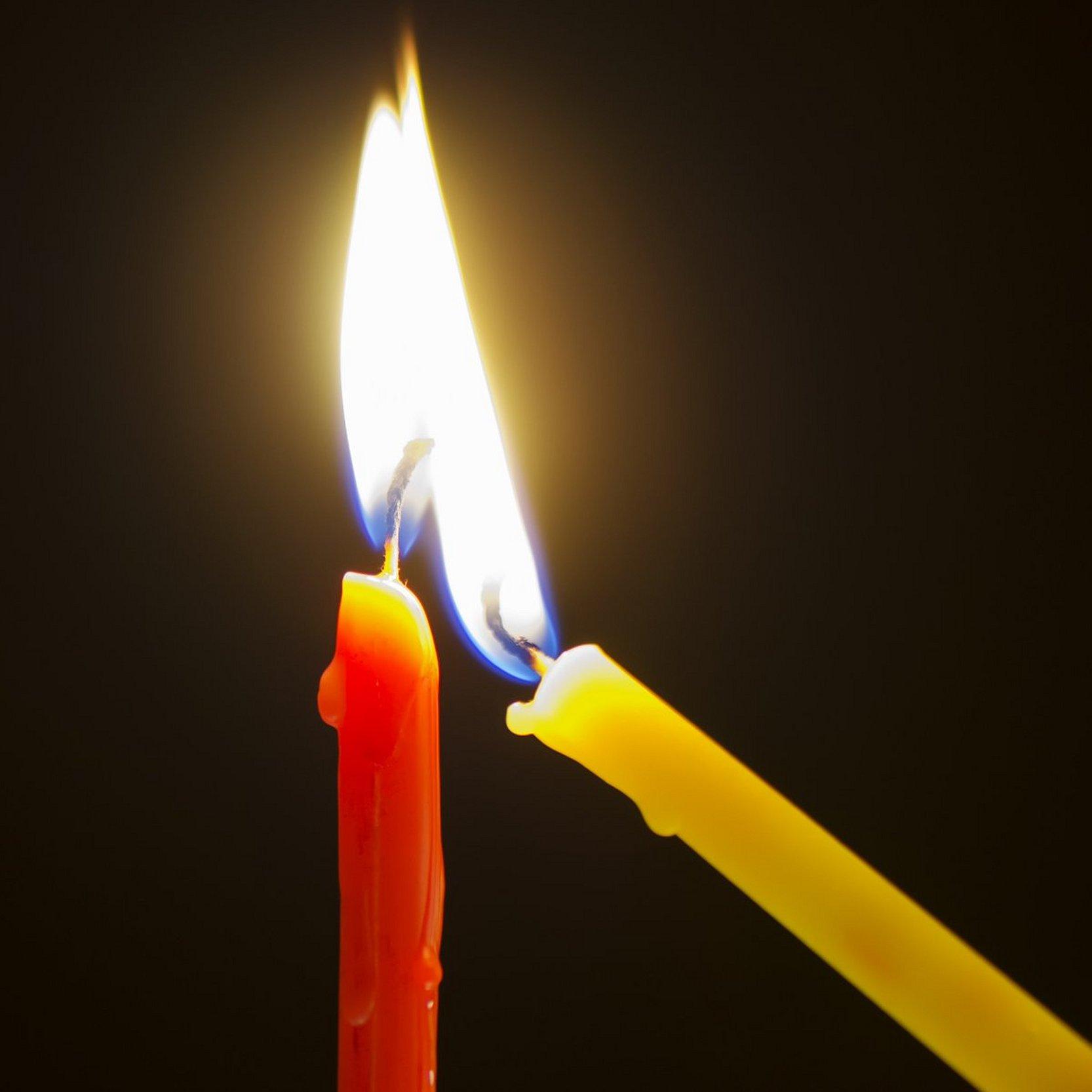 Segen geben und ein Licht empfangen Eine gelbe schmale Kerze wird an einer roten schmalen Kerze angezündet.