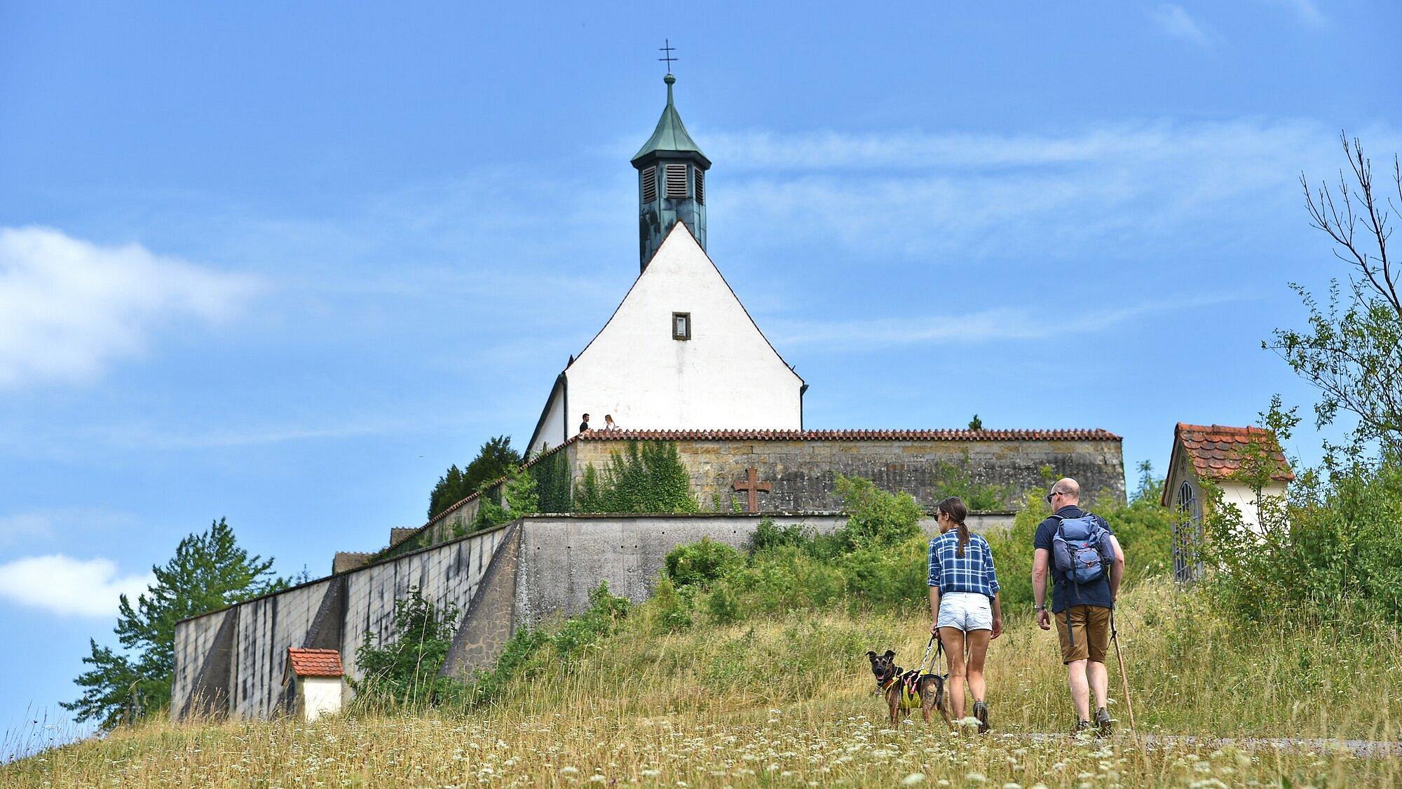 Ein Mann und eine Frau mit Hund an der Leine pilgern hoch zur Wurmlinger Kapelle
