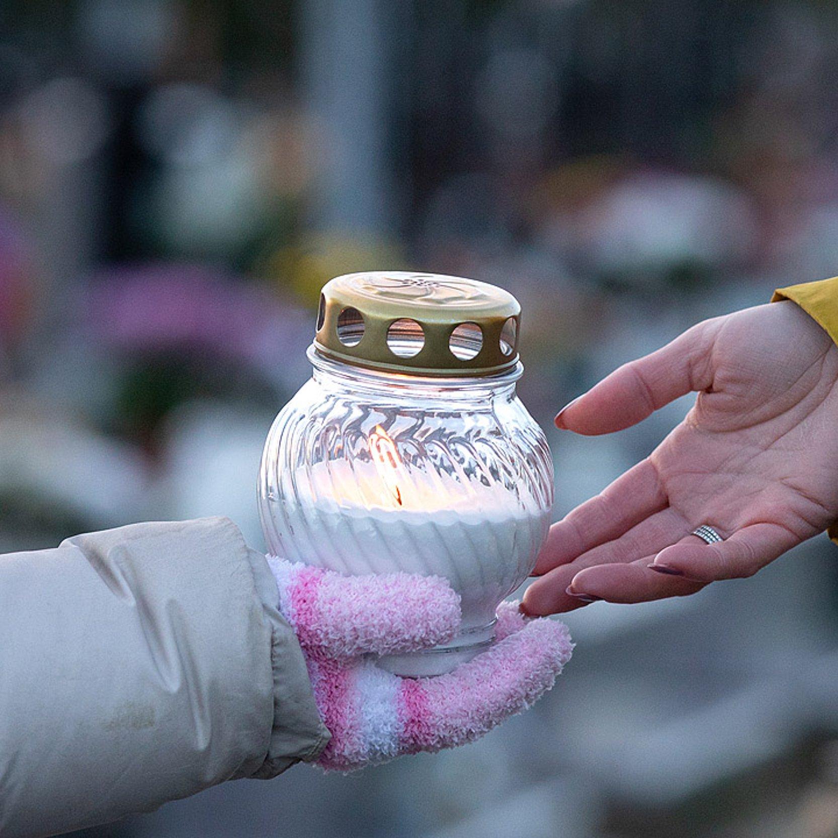 Kerze Ein Windlicht wird auf einem Friedhof von einer Hand in die andere weiter gegeben