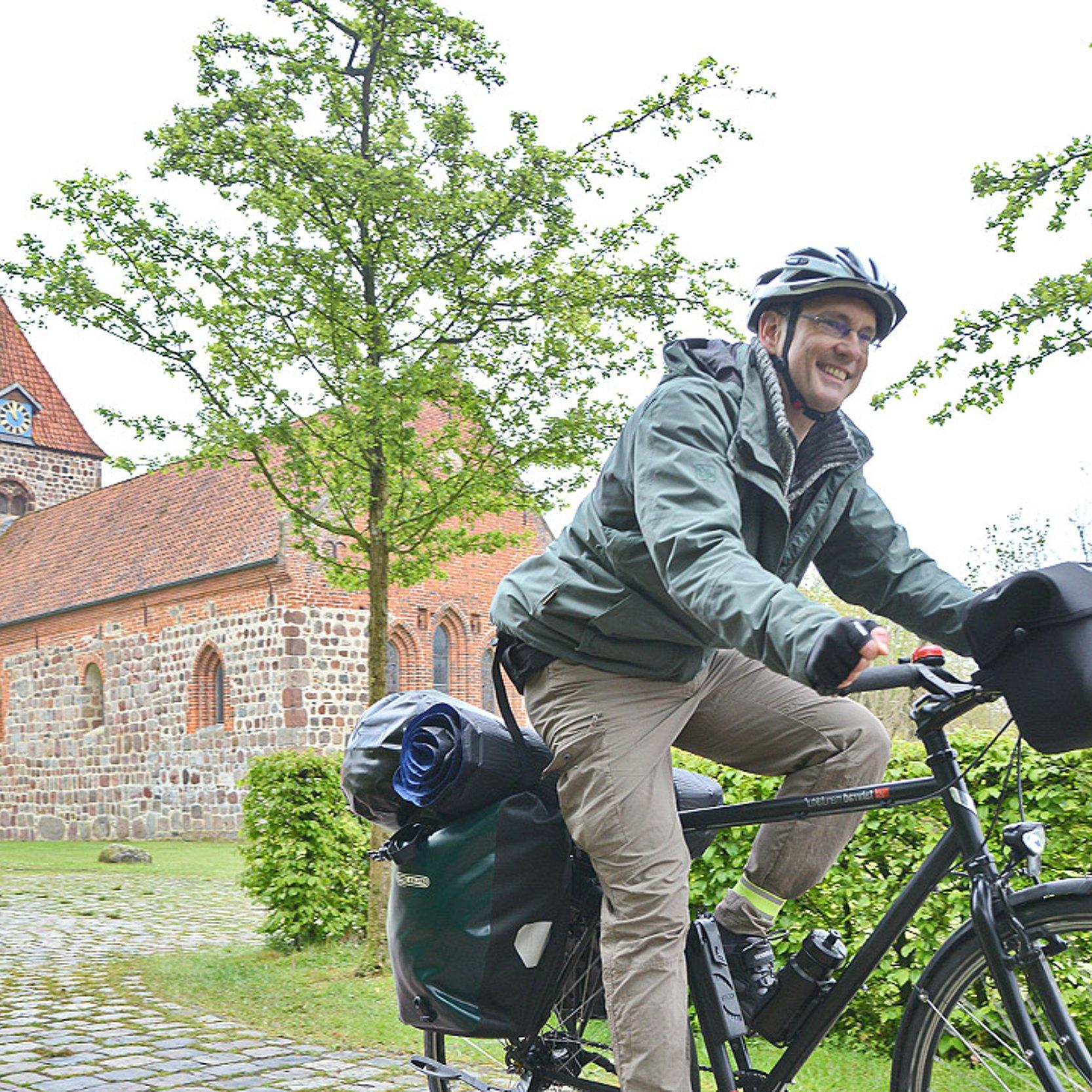 Radpilgern Ein Mann fährt Fahhrad, im Hintergrund steht eine Kirche