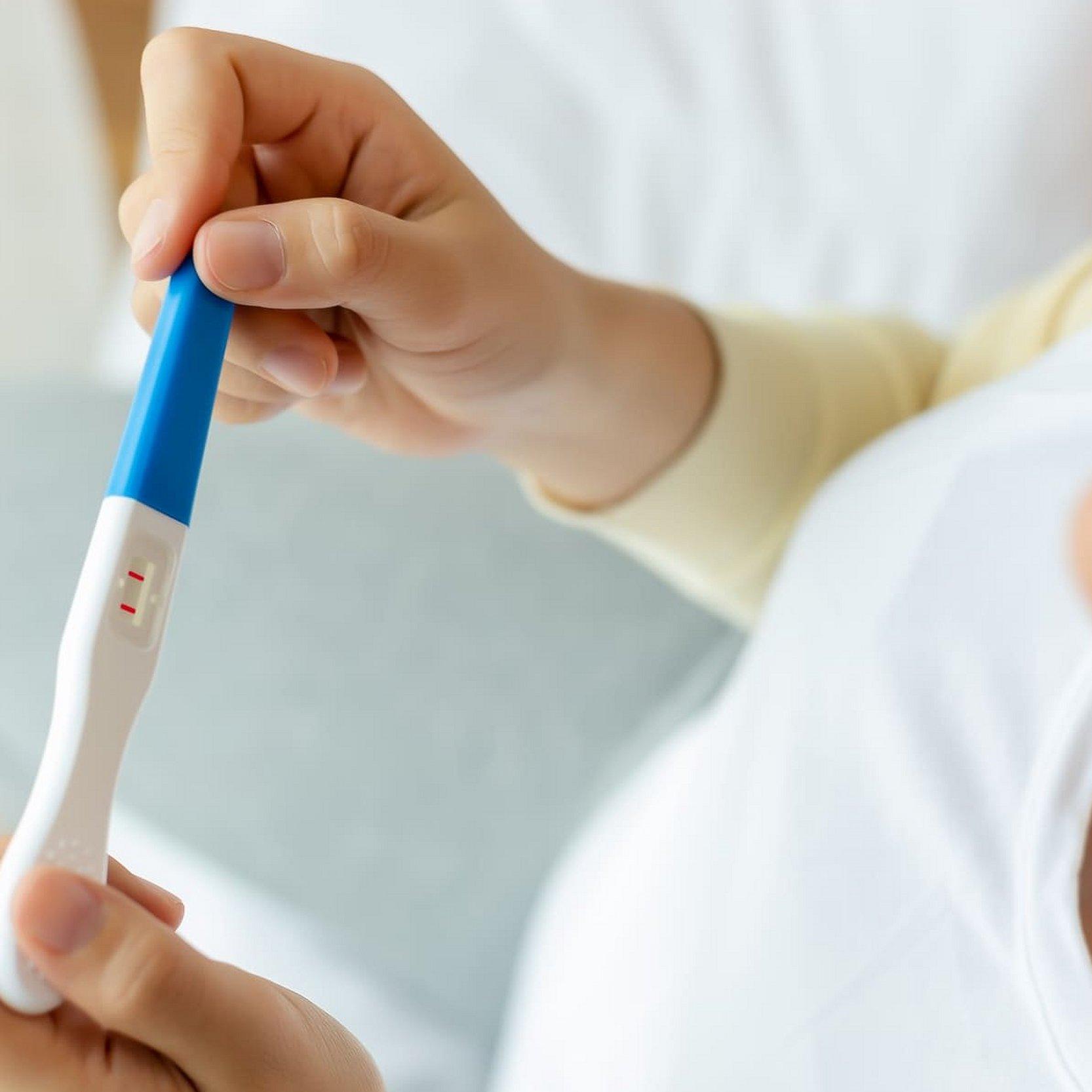 Diakonie Schwangerschafts- und Schwangerschaftskonfliktberatung Eine Frau hält einen positiven Schwangerschaftstest in ihren beiden Händen. Zwei rote Balken sind auf dem Sichtfeld zu erkennen.