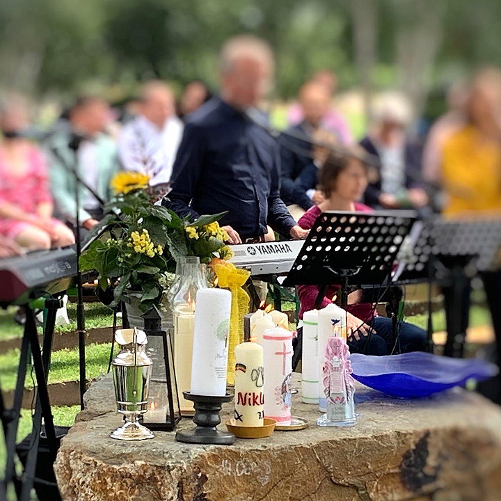 Tauffest in Bingen Ein Tauffest findet draußen statt. Auf einem Fels stehen mehrere Taufkerzen im Hintergrund spielt eine Band Musik.
