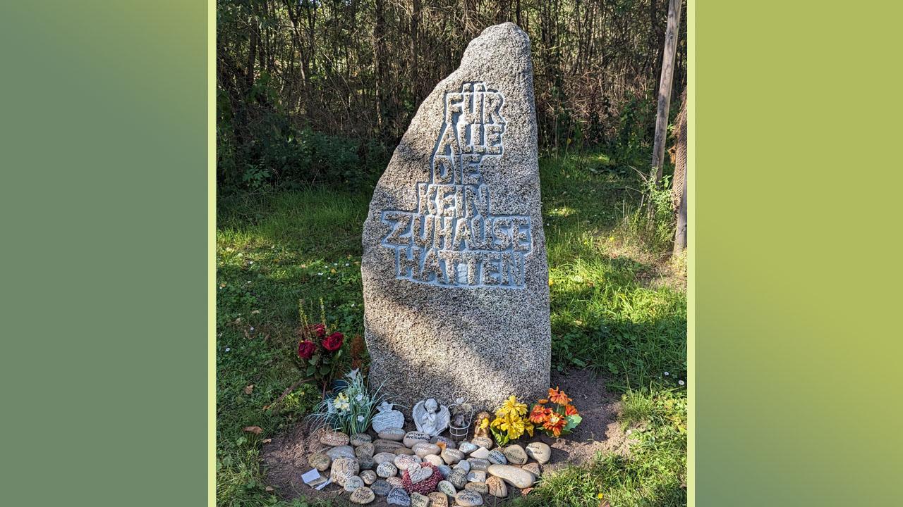 Gedenken an Obdachlose Gedenkstein mit kleineren Steinen davor und Blumen