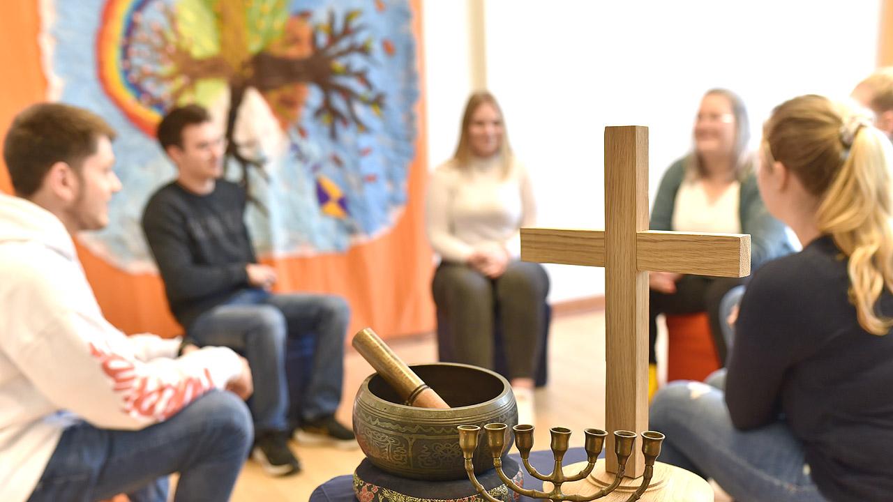 Oberstufenschüler sitzen im Kreis, davor sind ein christliches Kreuz, eine Klangschale und ein siebenarmiger Leuchter