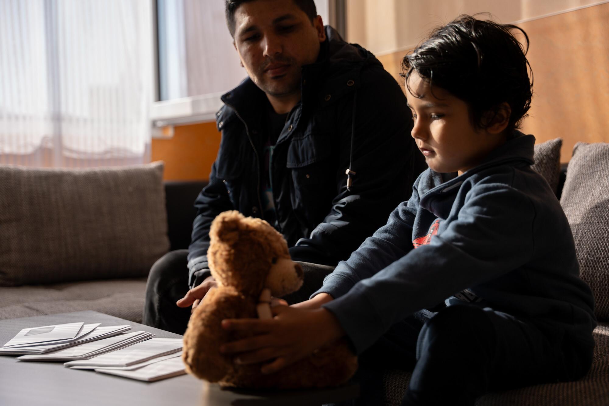 Vater und Sohn im Wohnzimmer Vater und Sohn sitzen im Wohnzimmer, Sohn spielt mit Teddy