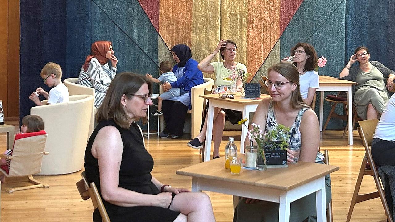 Menschen, die an Tischen sitzen in einem Kirchenraum, der mit Holz ausgekleidet ist