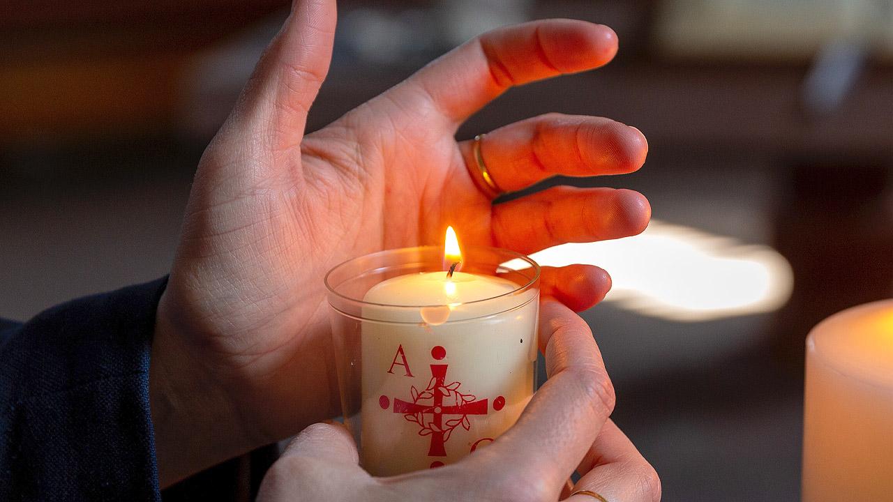 Hand hinter einer kleinen Osterkerze