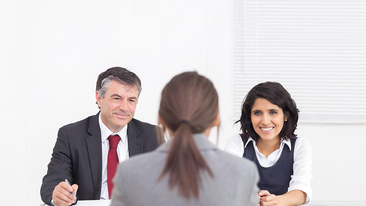 Eine Bewerberin sitzt vor zwei Menschen, die das Bewerbungsgespräch führen